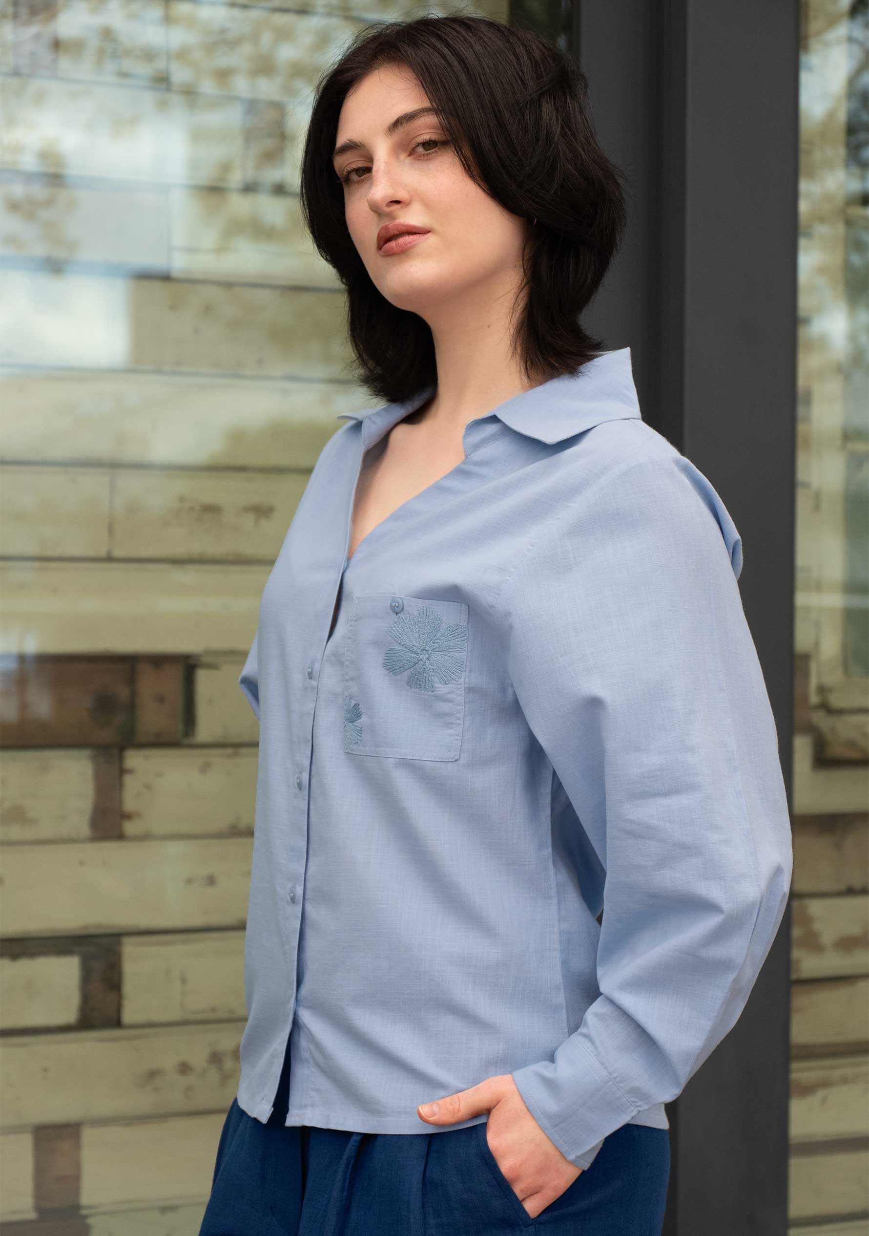 Close-up of hand-embroidered tonal floral detail on chest pocket of powder blue handloom cotton shirt; Detailaufnahme der handbestickten Ton-in-Ton-Blüten an der Brusttasche einer puderblauen Bluse aus handgewebter Baumwolle