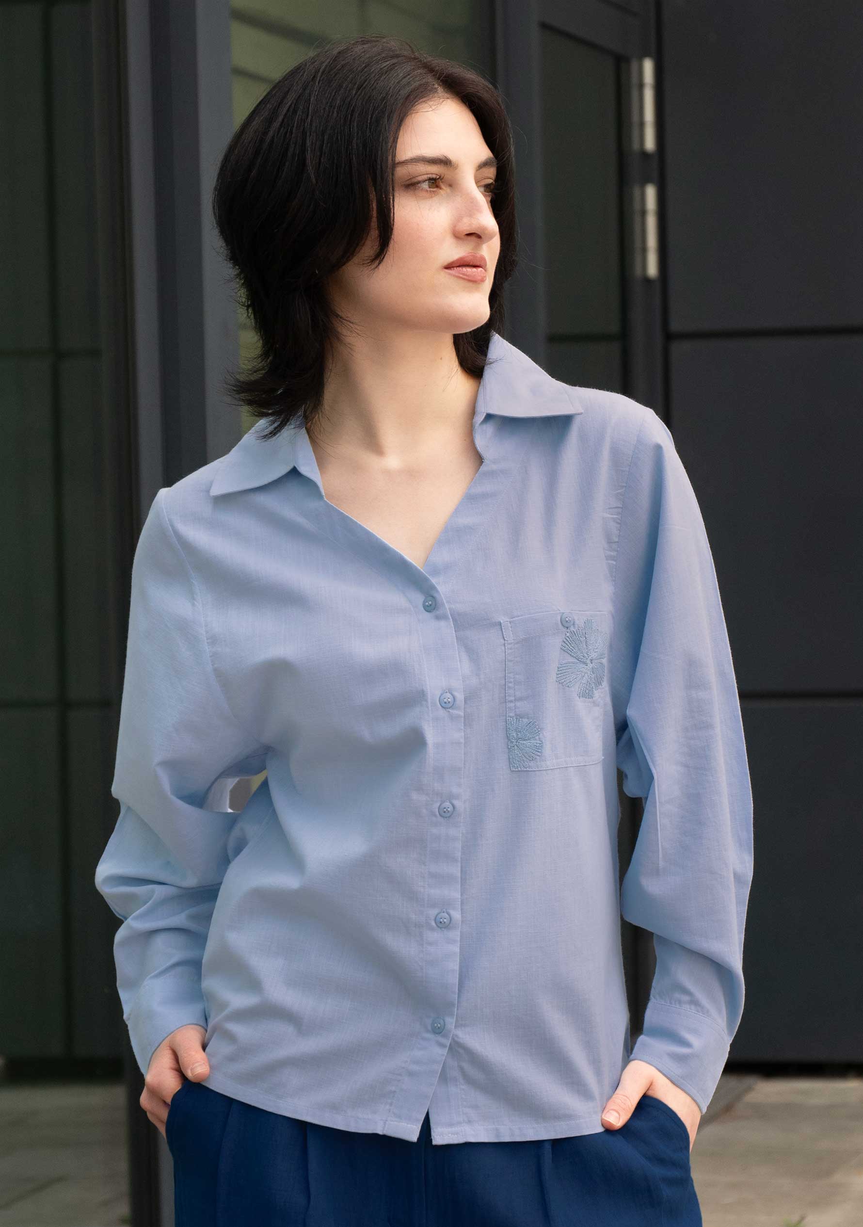 Women's light blue cotton shirt with hand-embroidered floral detail on chest pocket and open convertible collar; Damenbluse in Puderblau aus Baumwolle, handbestickte Blütendetails an der Brusttasche, offener Kragen